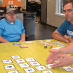 Joe seated at table with co-workers playing a card game