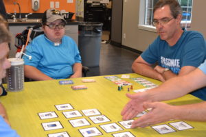 Joe seated at table with co-workers playing a card game