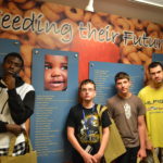 Four teens pose in front of mural at the Food Bank.