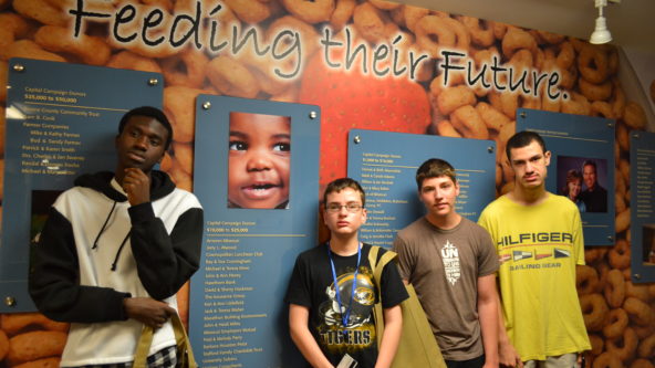 Four teens pose in front of mural at the Food Bank.