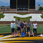 Teens and teachers pose for a picture on the MU football field.