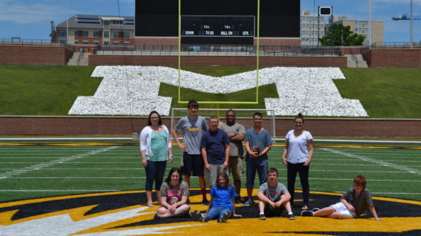 Teens and teachers pose for a picture on the MU football field.