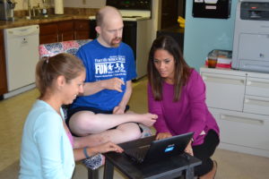 A man sits and watches as two staff members set up a laptop for a skype call