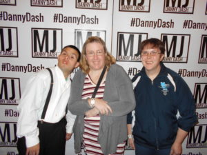 Three people pose in front of the backdrop for the concert.