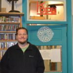 Matt stands in front of the office door at the radio station.