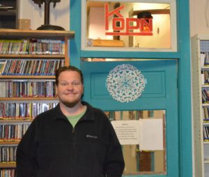 Matt stands in front of the office door at the radio station.