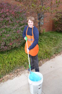 Alex holds a mop in a bucket.
