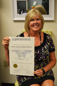 Robyn holds up the certificate for the three-year accreditation from CARF International.