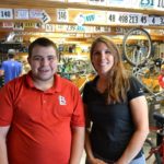 Aaron stands next to Sarah in the bike shop.