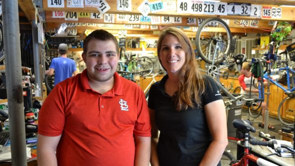 Aaron stands next to Sarah in the bike shop.