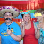 Kaitlyn poses with two of the individuals she supports. They are in a photo booth with fiesta-themed photo props.