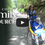 A woman guides a duet bike carrying an older woman with a disability.