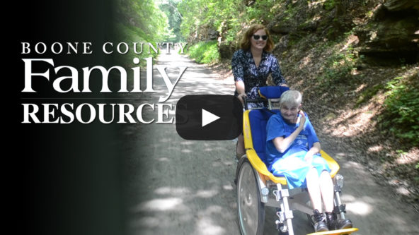 A woman guides a duet bike carrying an older woman with a disability.