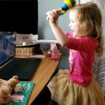 Young girl gleefully shakes maracas looking at computer.
