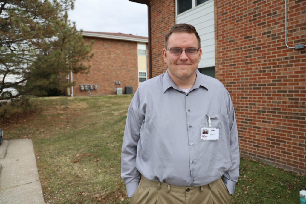 Dale stands outside his apartment dressed professionally for work.