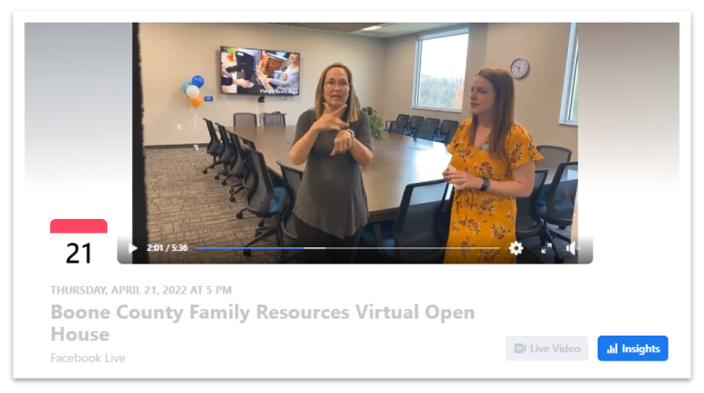 An ASL interpreter signs behind a young woman giving a board room tour live on Facebook. 