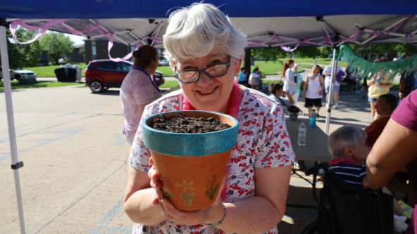 A woman with glasses and grey hair holds a hand painted pot with dirt.
