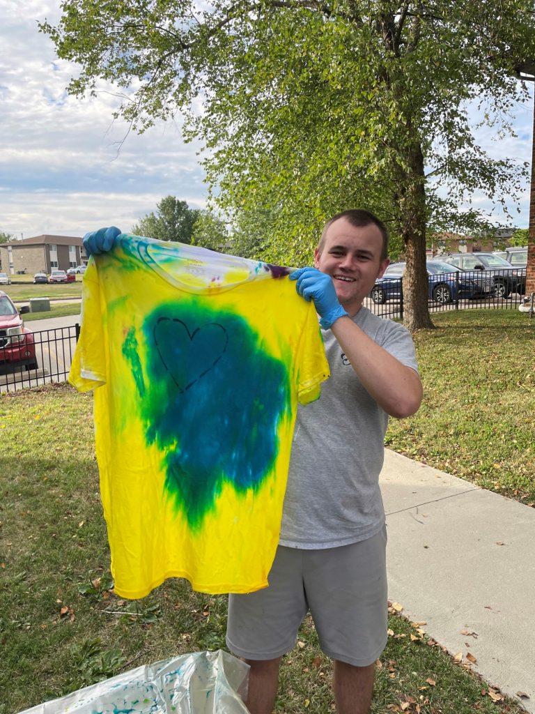 A man holds up a bright yellow and blue tie dyed t-shirt still dripping wet.