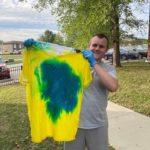 Man holds up a yellow and blue tie-dyed t-shirt.