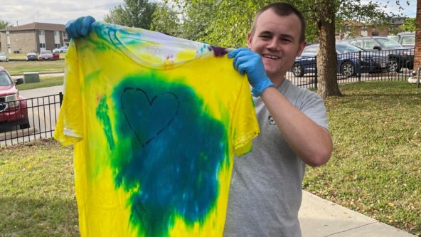 Man holds up a yellow and blue tie-dyed t-shirt.
