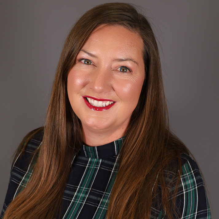 A caucasian woman with long brown hair wearing a green plaid high neck shirt.