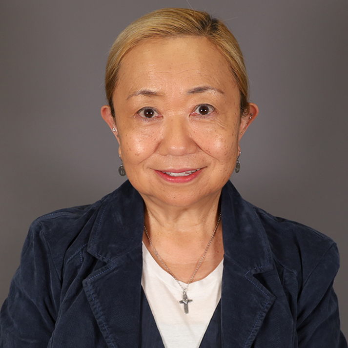 Asian woman wearing a navy velvet suit with very short light hair.