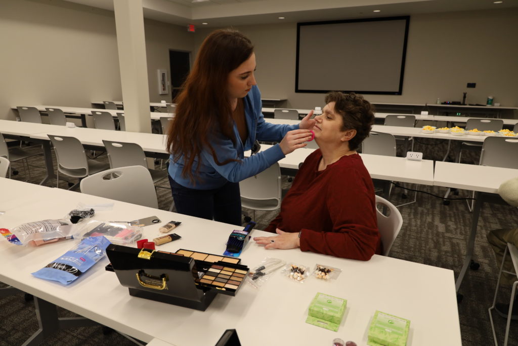A staff member puts makeup on a seated individual.