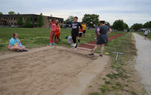 Leo is jumping into a sand pit at the Special Olympics track and field practice.