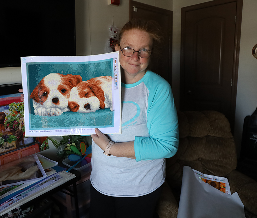 Tina holds up a canvas featuring puppies made of very tiny colored diamonds.