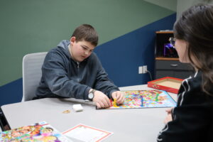 Jaxon sitting at the designated table to play CandyLand with staff member. 