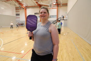 Dena poses for a closeup photo holding her pickleball paddle. She is wearing atheletic clothes.