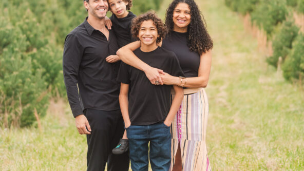 A family of 4 stand in a field hugging for a family photo.