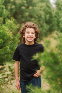 A child poses for a portrait in a field, smiling broadly.
