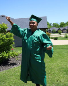 Drew throws his hand up in triumph while wearing his green cap and gown.
