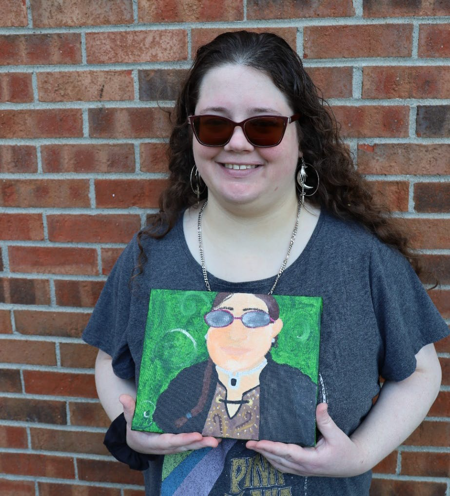 Kayla wears dark sunglasses and has long curly brown hair.